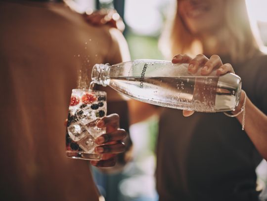 Kobieta nalewa wodę gazowaną z butelki SodaStream do szklanki z lodem i owocami.